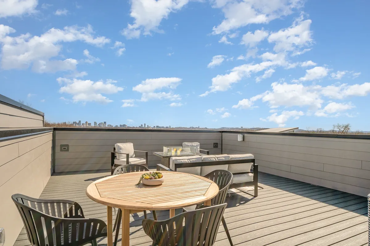 A tranquil rooftop patio with an outdoor seating area and a wooden table, set against the stunning backdrop of the city skyline. The mood is social and serene, ideal for group gatherings or quiet moments.