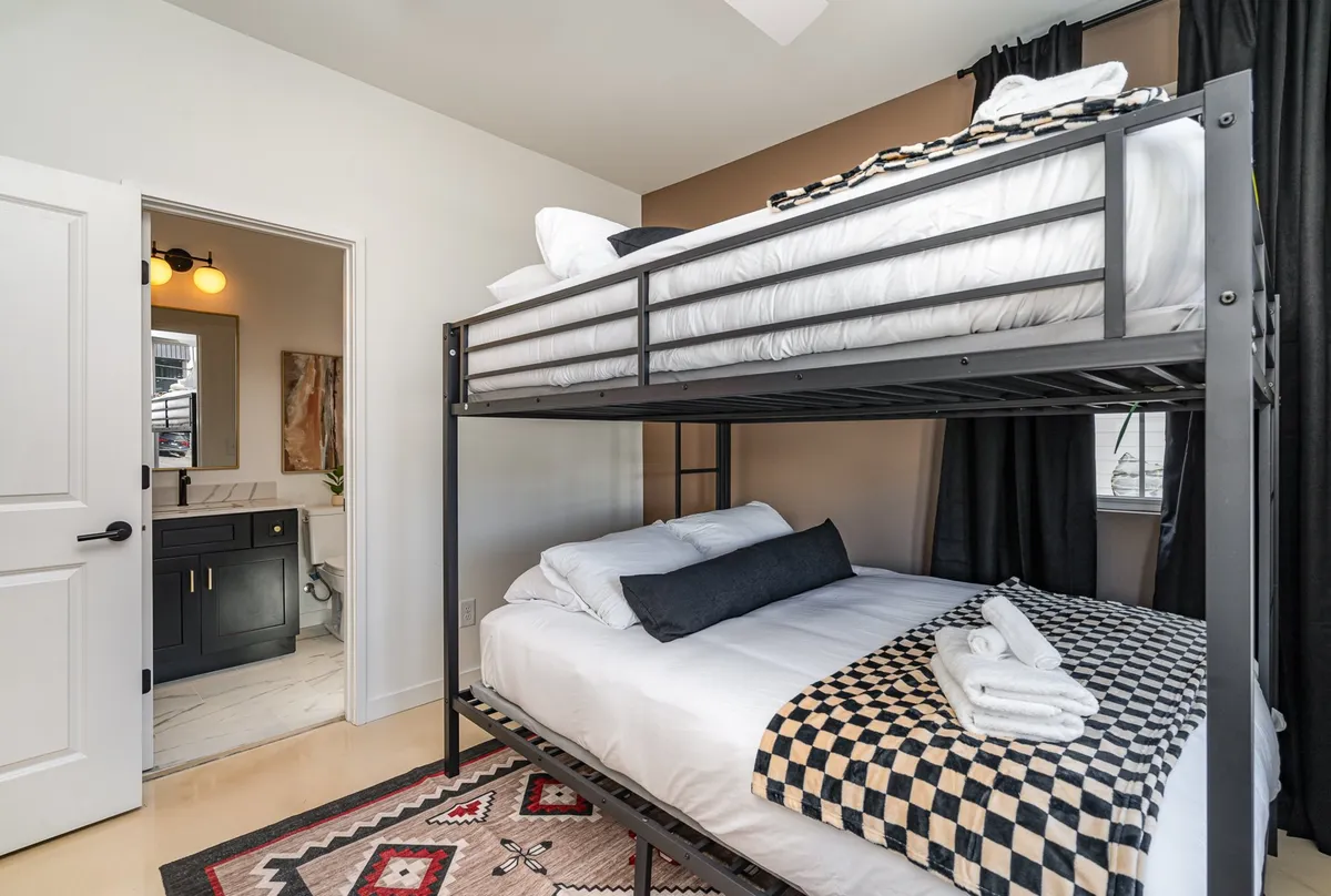 A cheerful interior bedroom with bunk beds, a decorative rug, and an adjoining bathroom entrance. The setup is perfect for groups or families, offering privacy and flexibility within the home.