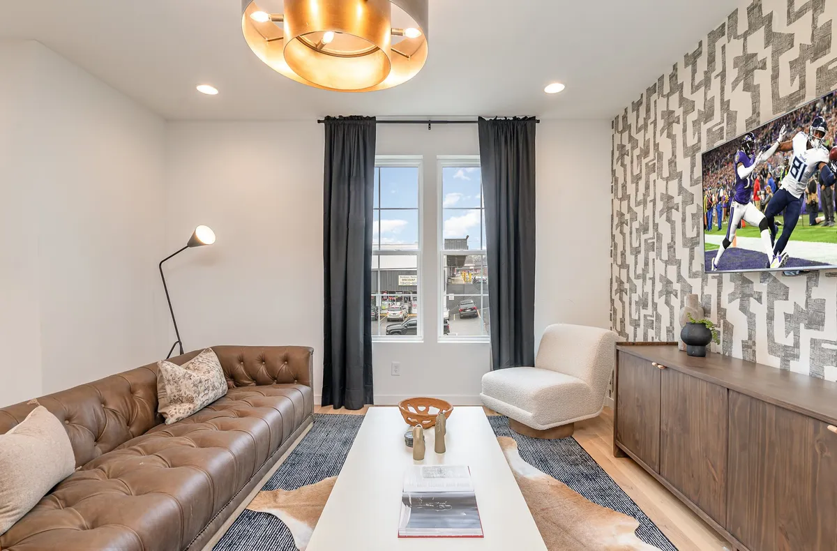 A cozy living room highlighted by a chocolate brown leather sofa, large framed television, a modern light fixture, and a sleek coffee table. The arrangement is perfect for unwinding after a day out or hosting a movie or game night, with ample space for guests to gather.
