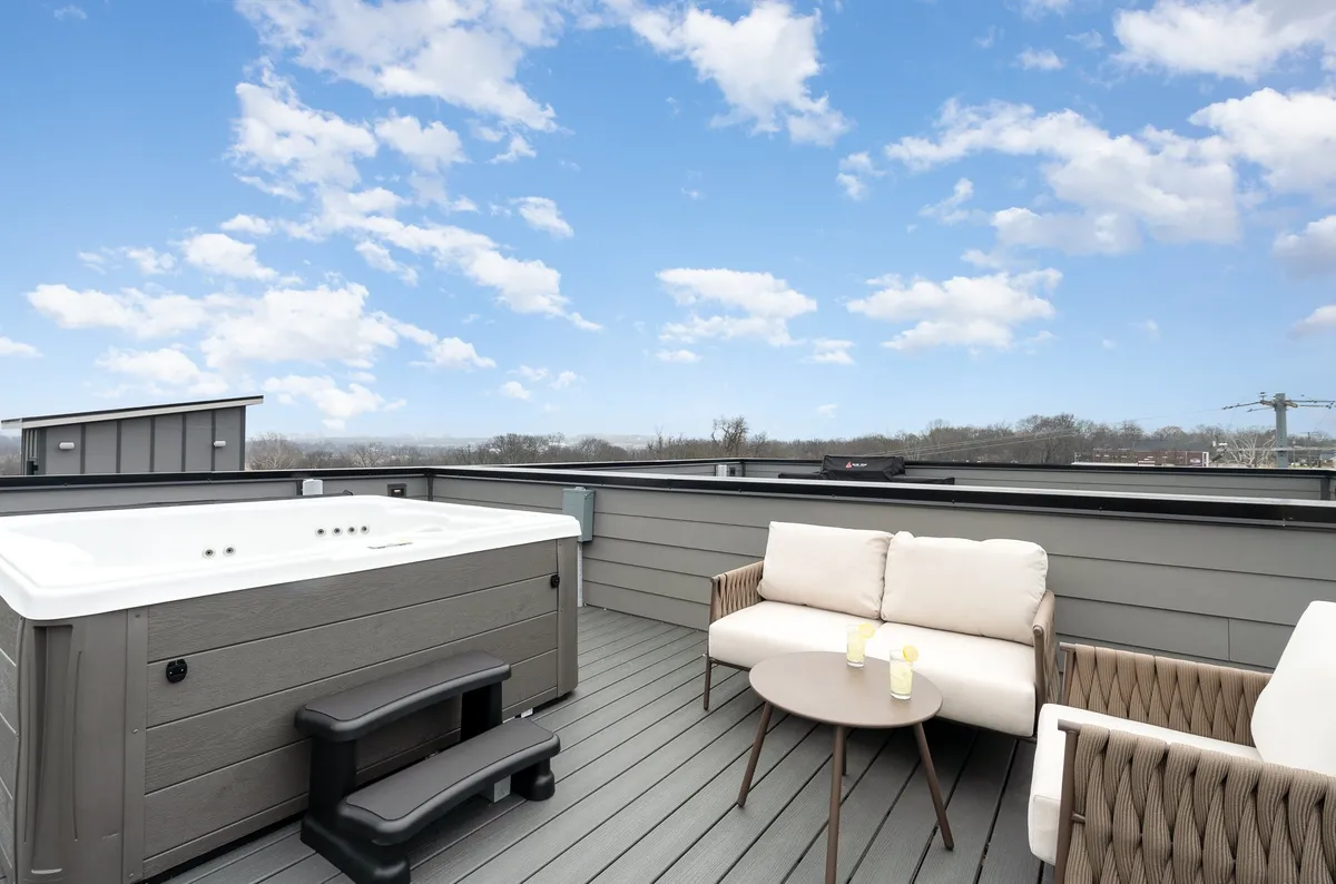 A private rooftop scene featuring a bubbling hot tub, contemporary outdoor seating, and an open blue sky. The area feels spacious and inviting, perfect for relaxing or socializing while taking in the views.