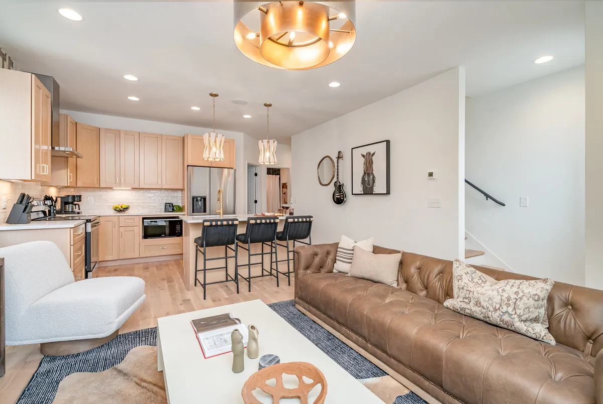 A contemporary open-concept living space featuring a comfortable sofa, a modern kitchen island, stylish lighting fixtures, and colorful artwork. The space is bright and welcoming, ideal for communal gatherings and entertaining.