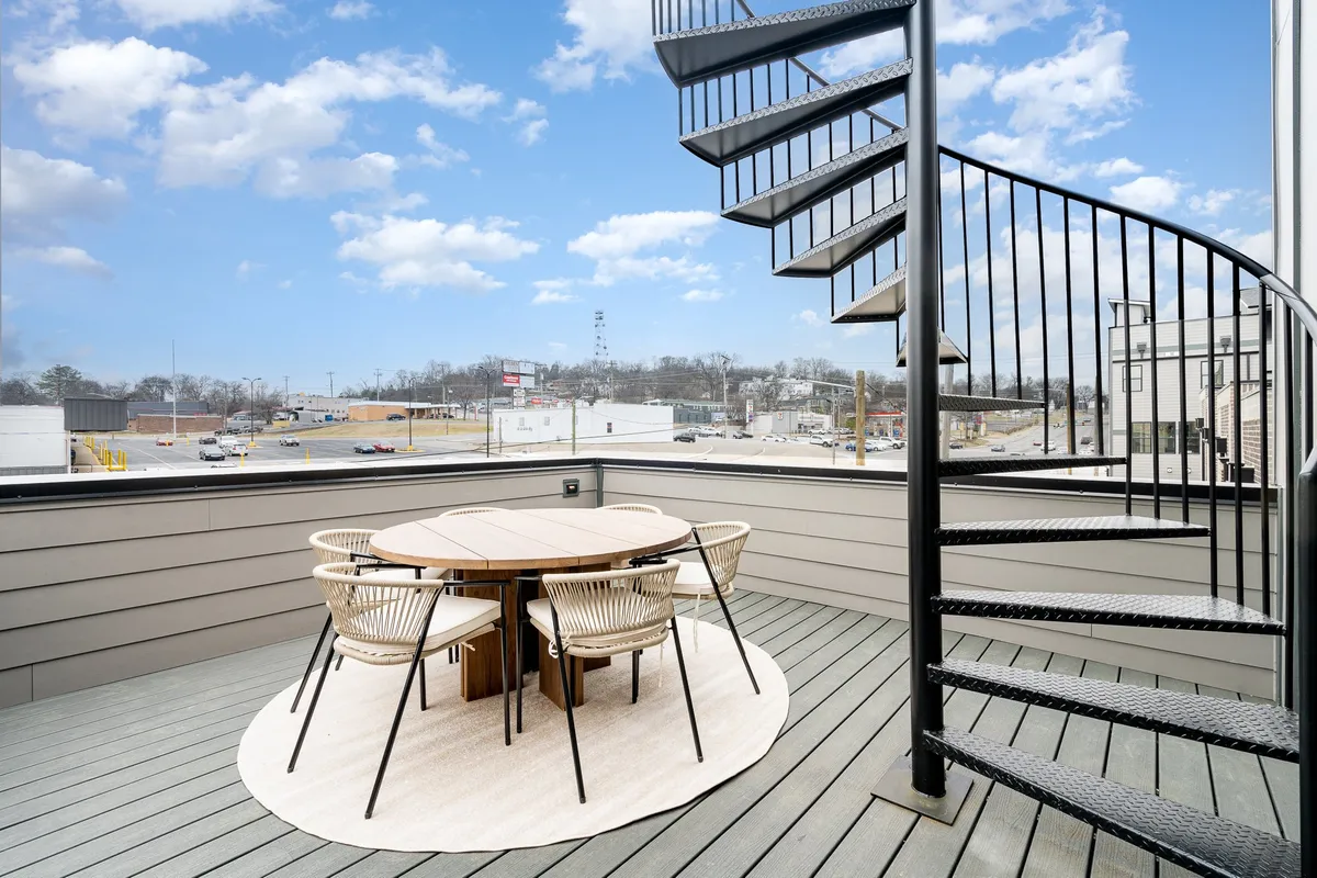 A rooftop level with a spiral staircase connecting upper and lower patios, a round dining table with woven chairs, and open-air ambiance for stargazing or sunset watching. The space is visually dynamic, offering both function and architectural interest.