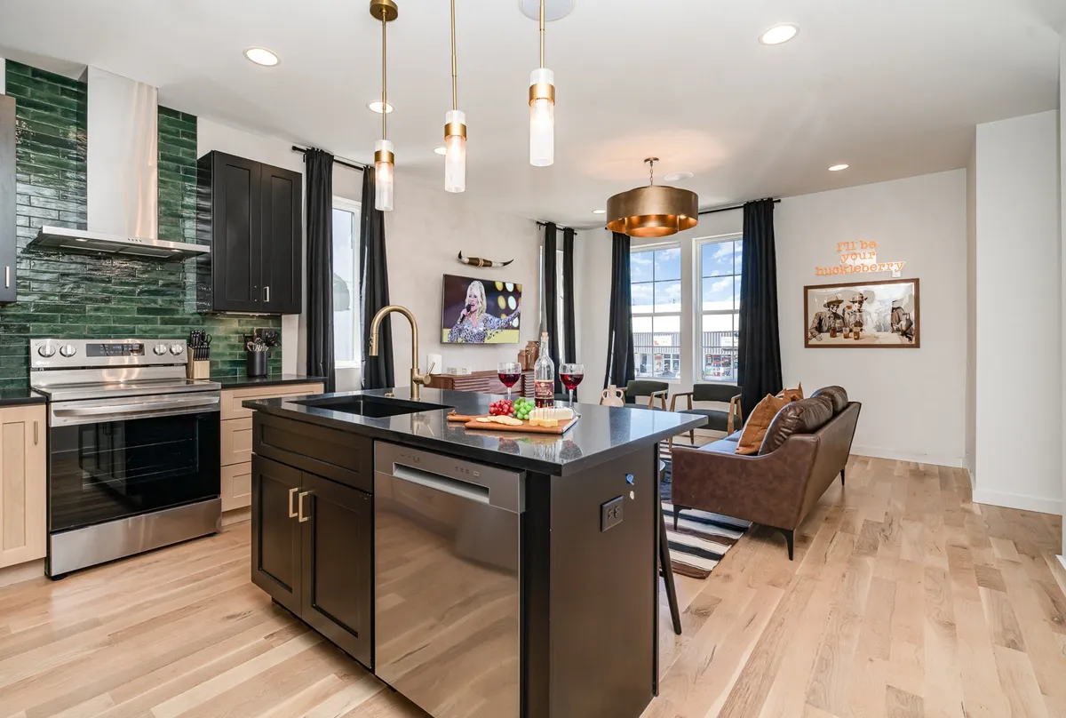 A wide, inviting view of an open-plan space featuring a kitchen island with bar stools, modern stainless steel appliances, a dining area, and vibrant artwork on the wall. The space is bathed in natural light and is arranged to encourage both cooking and social interaction. The sightlines extend from the kitchen through to the dining and living areas, showing seamless connectivity.