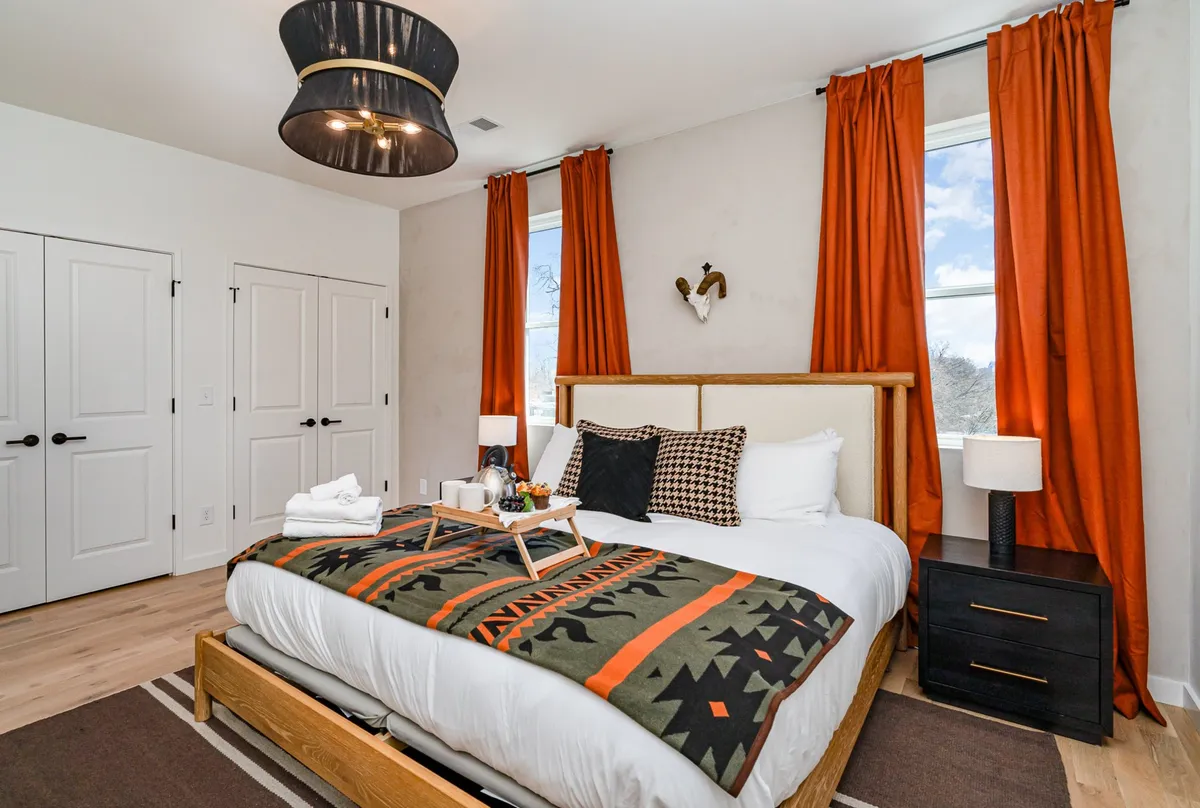A sunlit bedroom featuring a comfortable bed with a decorative blanket, elegant nightstands, and soft window curtains. The mood is warm and restful, inviting peaceful downtime.