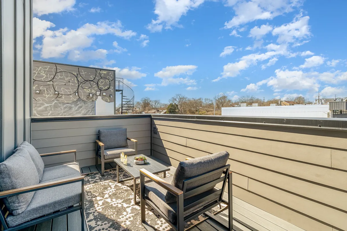 A rooftop patio with comfortable outdoor seating, a decorative rug, and an open view of the sky. The cozy arrangement invites relaxation and informal gatherings, ideal for socializing or brainstorming sessions with a panoramic city backdrop.