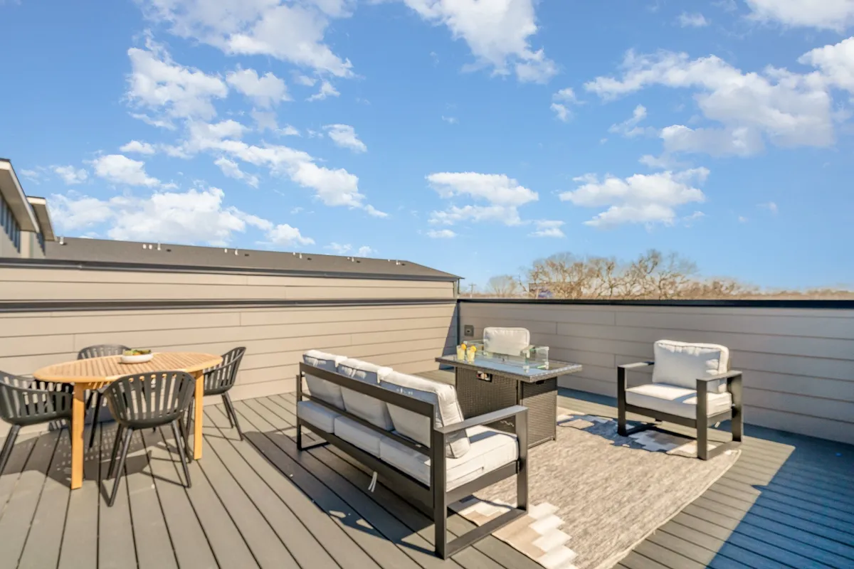This image features a cozy outdoor seating area with a dining table and decorative rug, perfect for enjoying a meal or a drink outside. The setting hints at opportunities for morning coffee or evening relaxation under the sky, evoking the feel of a private rooftop or terrace.
